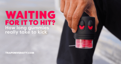 Hand holding Trap University jar with red HHC Gummies – text reads “How long gummies really take to kick in